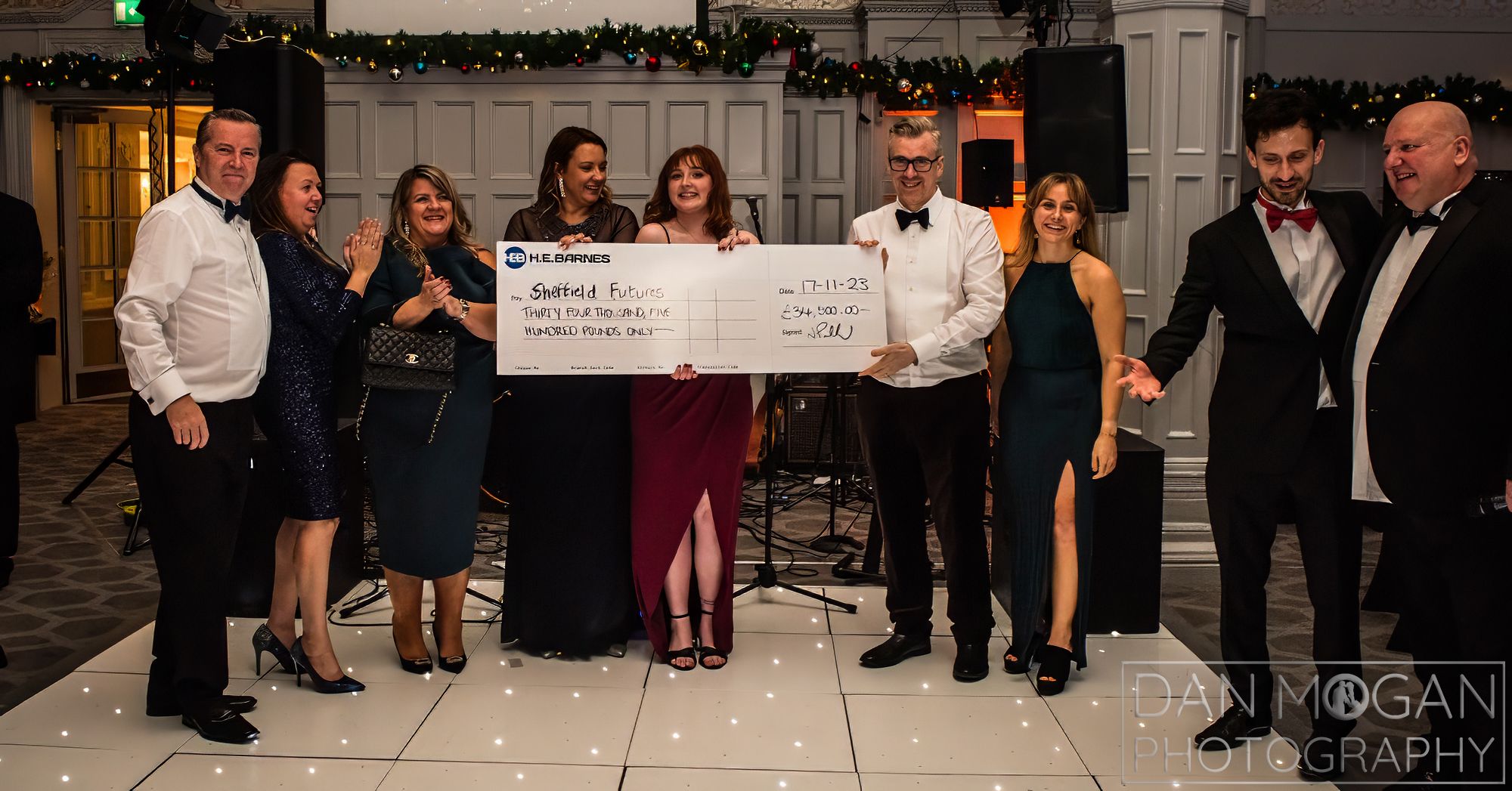 A photograph captures the moment the cheque was handed over. In this image, representatives from HE Barnes and Sheffield Futures are standing on the dancefloor smiling at the camera, holding the giant cheque.