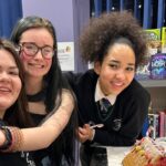 Three young people smile and hug each other, sat at a table in Wellbeing Cafe decorating gingerbread houses in the lead up to Christmas